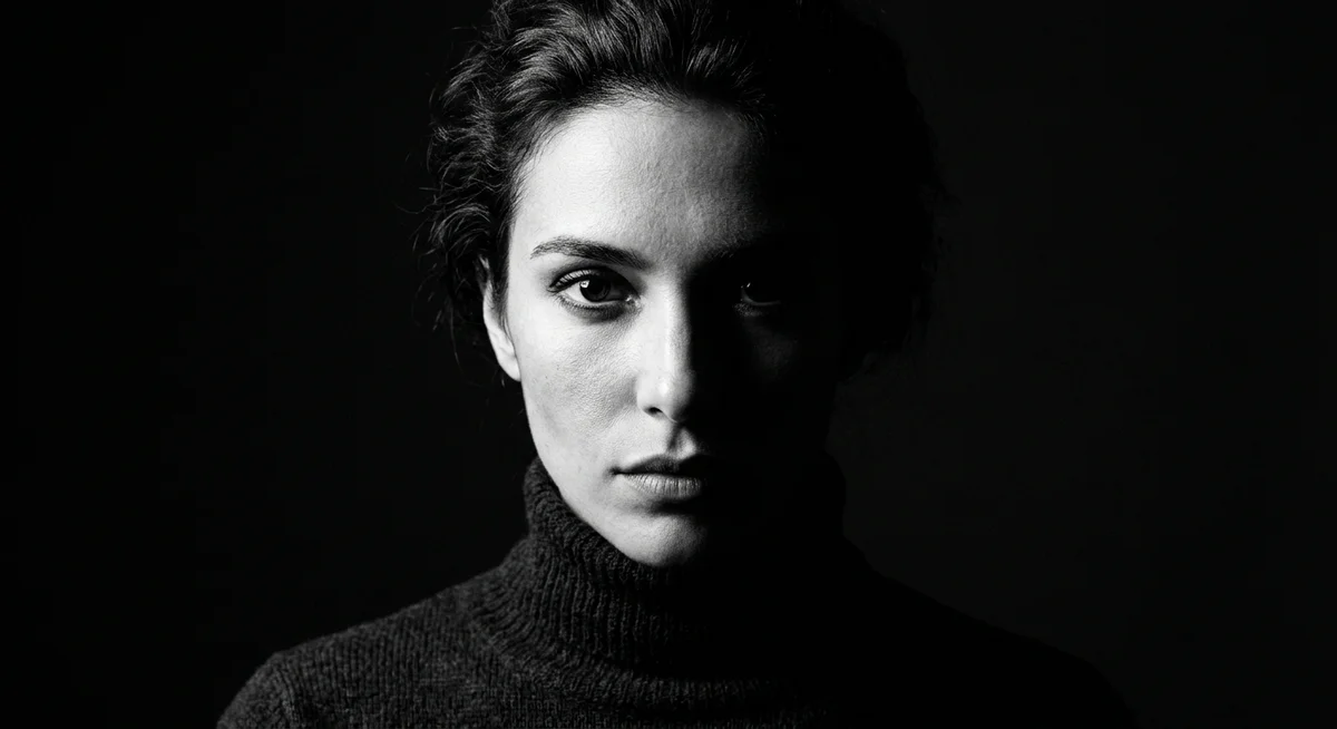 High-contrast chiaroscuro portrait of a woman in a ribbed turtleneck against a black studio background